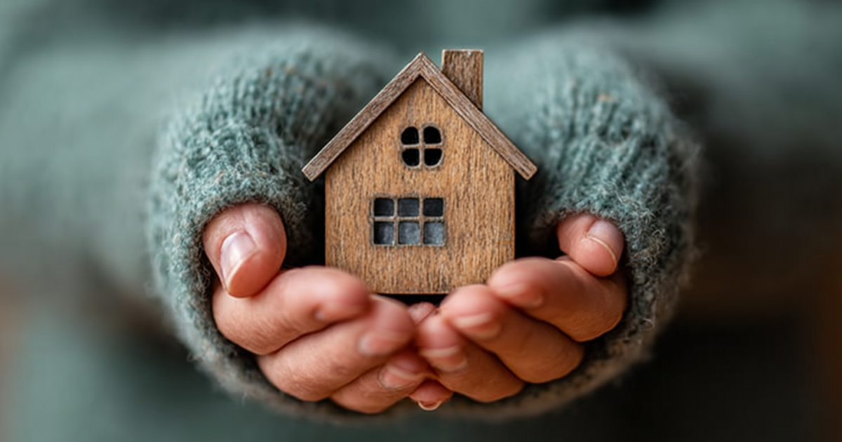 Handen die zorgvuldig een houten huisje vasthouden, symbool voor thuiszorg en sociale zekerheid